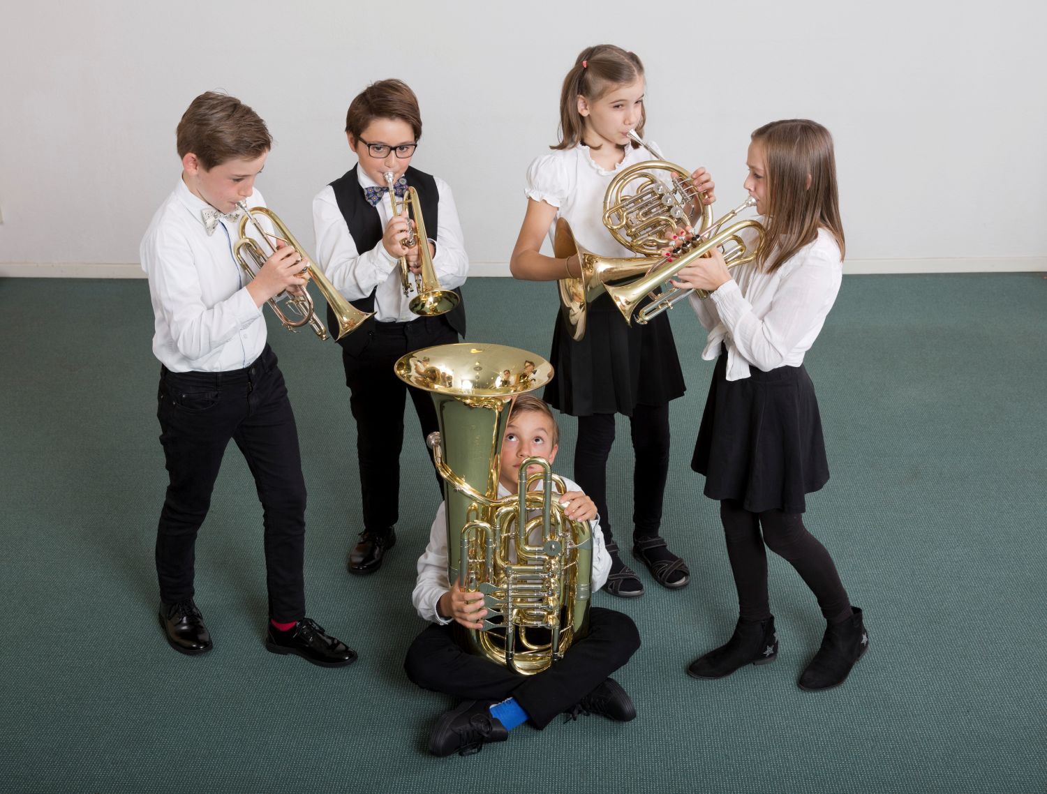 Fünf Kinder, davon eines sitzend spielen auf verschiedenen goldenen Blasinstrumenten