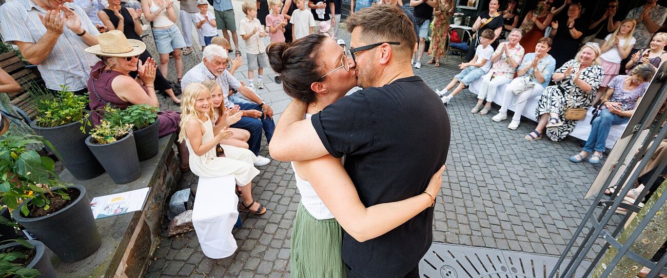 Frau und Mann küssen sich im Hintergrund viele Menschen auf einem Marktplatz die zuschauen
