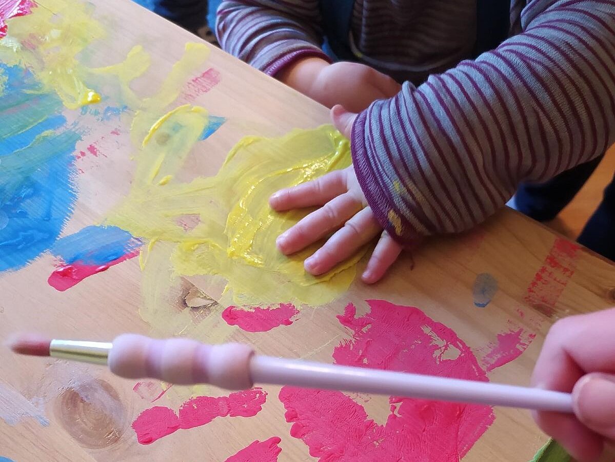 Eine Kinderhand macht mit Farbe einen Abdruck auf einem Holzsarg