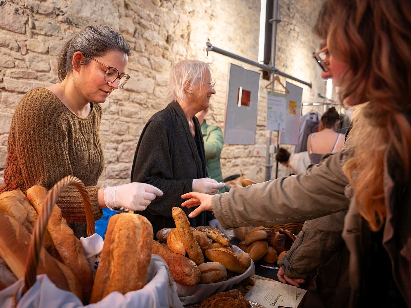 An einem Tich verteilen zwei Frauen Brote und Brötchen an mehrere Menschen.